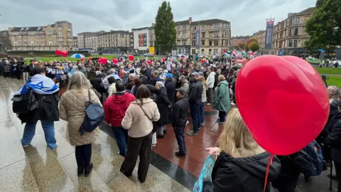 A photo of a crowd gathered at Kelvingrove museum. Some are holding red heart shaped balloons.