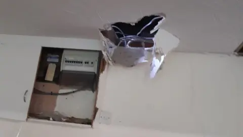 Stone Town FC A white ceiling with a large hole in it and wires sticking out. The electrical cupboard can be seen mounted on the wall behind.