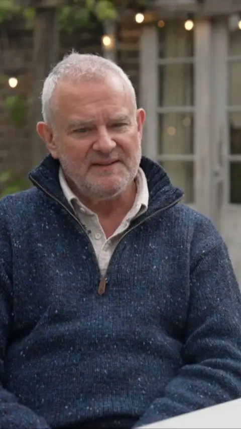 Actor Hugh Bonneville wearing a blue jumper sat outdoors
