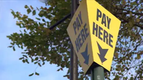 A yellow box with the words 'PAY HERE' with an arrow below. There are tree branches above it.