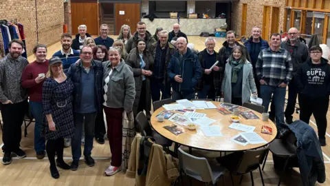 Louis Reynolds/BBC A group of actors and directors stood in front of the stage at Great Ouseburn village hall in their first meeting to discuss putting on a pantomime. 