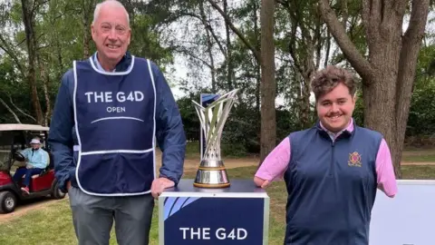 Adam is standing on the right of the G4D tournament trophy with an older men to the left.