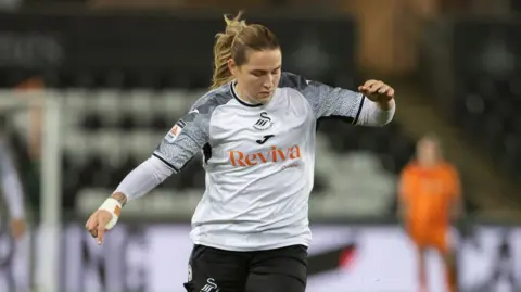 Getty Images Chloe is wearing black and white Swansea football kit. There are two players blurred in the background.