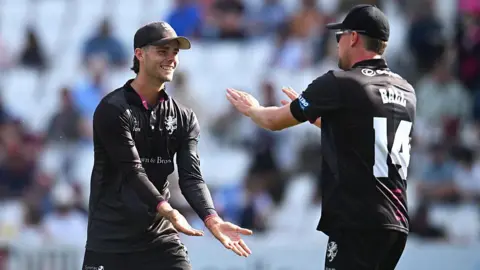 Getty Images Two Somerset cricket players in their black kit are high-fiving.