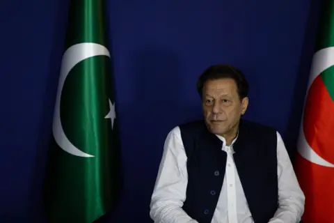 Getty Images Imran Khan sitting next to a Pakistan flag