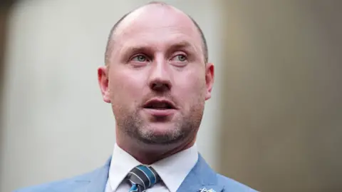 Neil Gray head and shoulders shot in blue suit and stripe tie