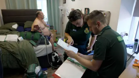 BBC Two paramedics visit a middle aged man who is struggling to breathe. He has an oxygen mask on while the paramedics check his notes