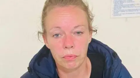 South Wales Police Charlene Hobbs staring expressionlessly forward, wearing a blue coat and with her light hair pulled back, against a light-coloured wall