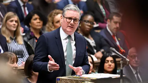 UK Parliament Prime Minister Sir Keir Starmer with grey hair and black framed glasses wearing a pale shirt, greyish green tie and navy suit speaking during Prime Minister's Questions in the House of Commons on Wednesday.