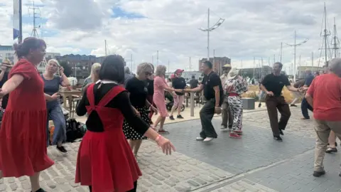 A group of people dancing next to Hull Marina.