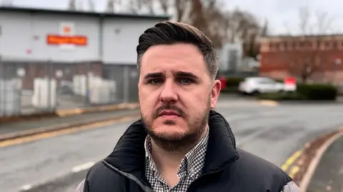Leigh Whitehouse standing on the side of the road, in front of the Royal Mail Delivery Office in Kidderminster