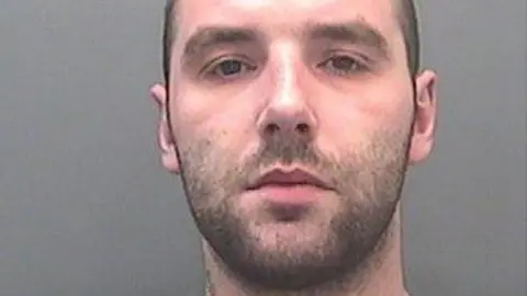 A custody image of David Braddon. He has dark stubble and looks at the camera with a neutral expression. 