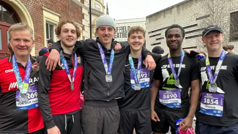 Five teenage boys and one man pose together with their arms around one another. They are wearing sports gear and medals.