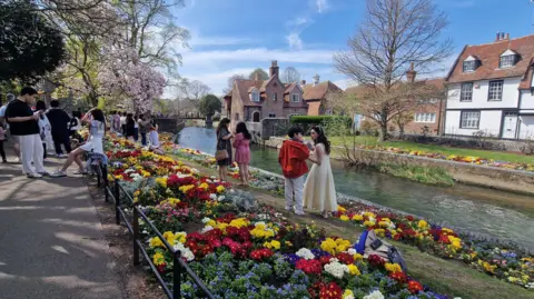BBC/JULIA ABBOTT A long view of the flower beds, with scores of people walking beside them and Westgate Towers in the background, and the River Stour beside it.