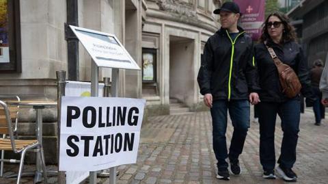 A man and woman standing near a polling station sign