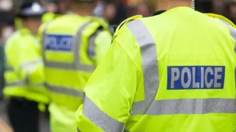 Three police officers, not in sharp focus, can be seen wearing yellow fluorescent jackets  