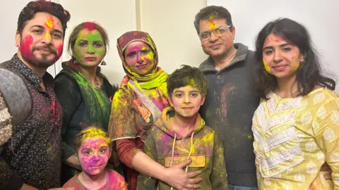 A family dressed in Indian outfits and covered in coloured powder 