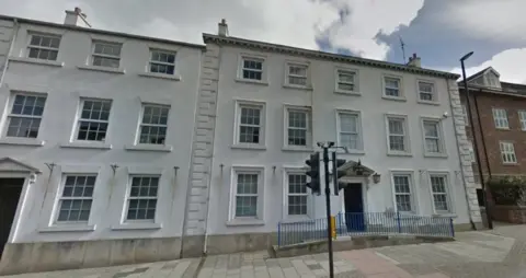 Google  A row of Georgian buildings with several rows of windows. Two of the buildings are white - one on the far left is brick built. 