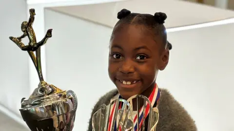 BBC Lauren Larbi wearing medals and holding two gymnastics trop