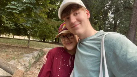 Supplied Abbie and Ethan in a park. They both wear caps and look like they are having a lovely day.