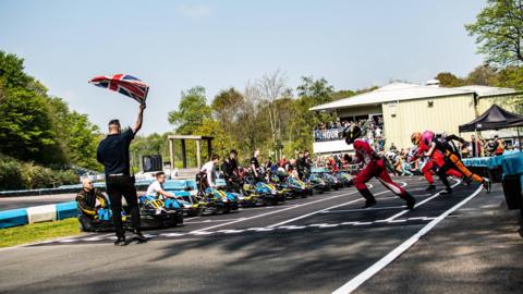 Young kart drivers race across the track to get into their karts at Buckmore Park as a man waves a 