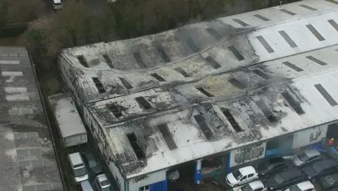 Cambs Police An aerial shot show a charred and partially collapsed metal roof on a large warehouse. There are cars and a lorry parked around the sides of the building