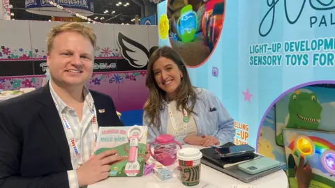 Danielle Kaye/BBC Two people pose at a booth at a Toy Convention.