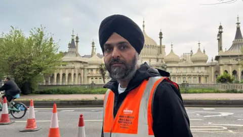 A man wearing an orange high-vis vest stood in front of the Brighton Pavilion
