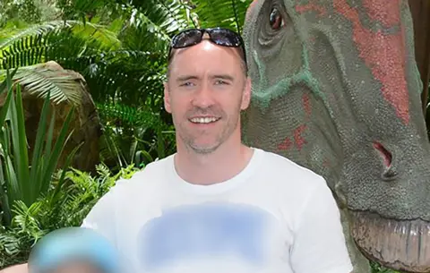 BBC Man smiling at the camera wearing a white t-shirt and sunglasses on his head. 