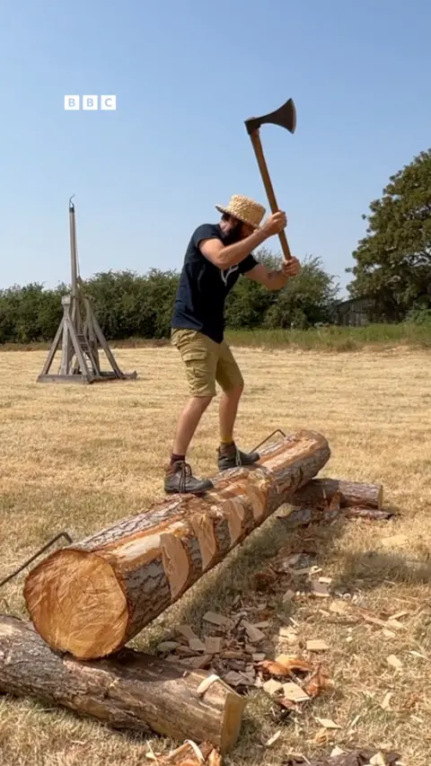 A man stands on a log holding an axe.