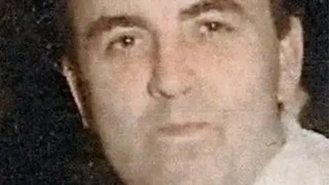 A faded picture of Joe Lynskey staring ahead into the camera. He has brown short brown hair and is wearing a white shirt