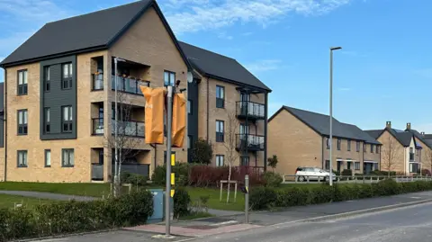 Eric Johnson/BBC New build houses on a clear blue day. Traffic lights are covered up in orange coverings. Roads look unfinished and have faded lines.