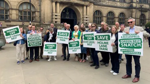 BBC/Lucy Ashton A group of people are standing in a line outside Sheffield town hall with large white and green placards