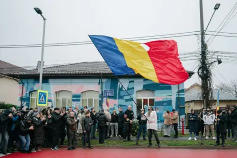 Getty Images A group of people stand in front of a colourful house as a man waves a giant Romanian flag