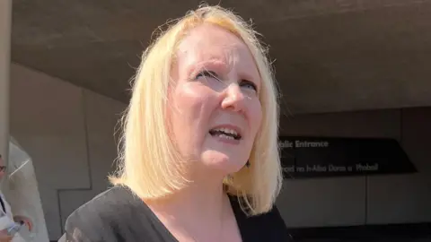 BBC Tressa Burke, who has shoulder length blonde hair looks off into the distance while standing outside the Scottish Parliament building in Edinburgh.