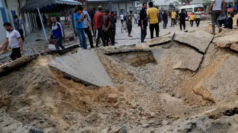A group of Palestinians stand by a large crater