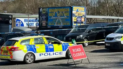 A police car and a road closure sign outside a garage in Bishopbriggs.