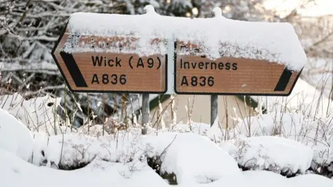 Snow sits on two road signs showing the way to Wick via the A9 on the left and Inverness on the right