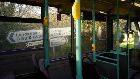 PA Media View from inside a bus, looking out at road signs. One sign pointing towards the back of the bus is to Land's End and ahead of the bus is Penzance.