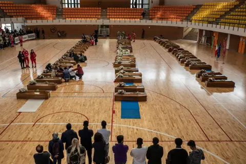 Getty Images Coffins lined up in a gymnasium in Crotone, Italy