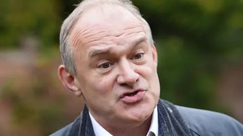 Liberal Democrats leader Sir Ed Davey, wearing a dark green jacket, is pictured speaking