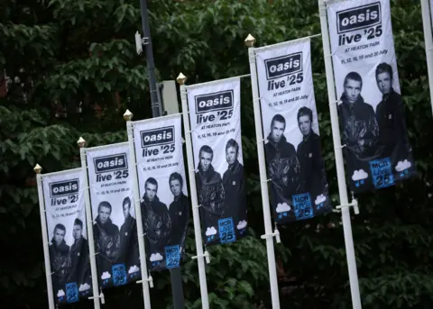 Oasis banners line the streets in Manchester ahead of the band's shows. The promotional banners are black and white with the band's Oasis logo at the top and an image of Noel and Liam at the bottom.