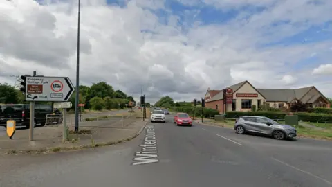 A road junction features incoming cars and a pub on the right side of the road