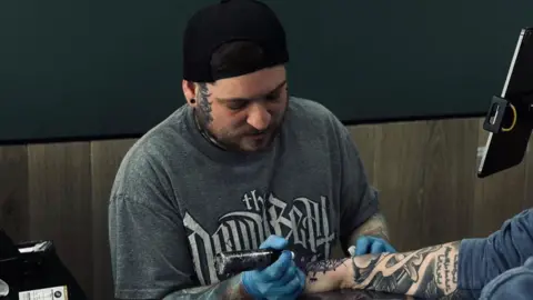 A tattoo artist doing a tattoo on someone's arm