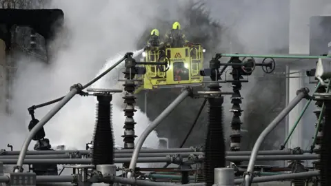 Getty Images Members of the Fire Brigade attend the scene following a major fire at an electrical substation at Heathrow on March 21, 2025 in London, England. A fire at the North Hyde electricity substation in Hayes has caused a significant power outage at Heathrow Airport leading to all flights in and out to be cancelled until midnight tonight affecting around 200,000 passengers. Some homes near to the fire have also been evacuated.