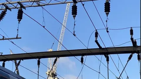 Network Rail Overhead rail wires against a blue sky. A white crane is in the background