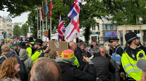 A group of people separated by police officers in hi-vis jackets. Some are holding Union Jack and St George's Cross flags.
