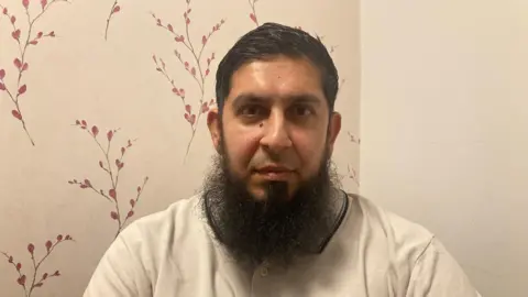 Charles Heslett/BBC A man with a long beard wearing a cream 