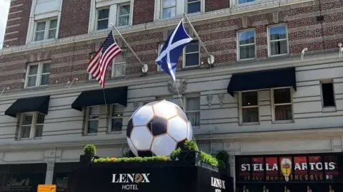 An American flag and a scottish flag hanging from a building on tip of a giant football