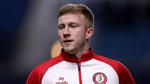 Ross McCrorie wearing a red and white Bristol City training jacket, looking towards his right 